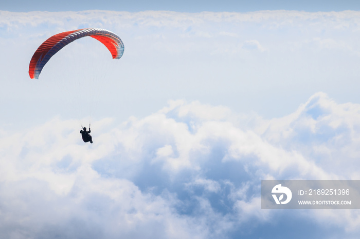 Paraglider flying over a sea of clouds during a sunny day.