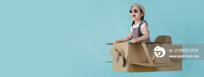 Asian little child girl playing with cardboard toy airplane handicraft isolated on blue long banner 