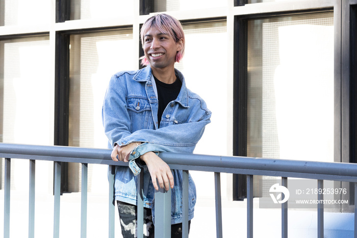 Non-binary person posing next to a railing.