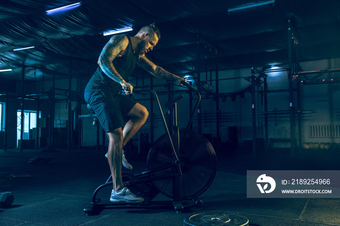 Young healthy man athlete doing exercise with the exercycles in gym. Single male model training hard