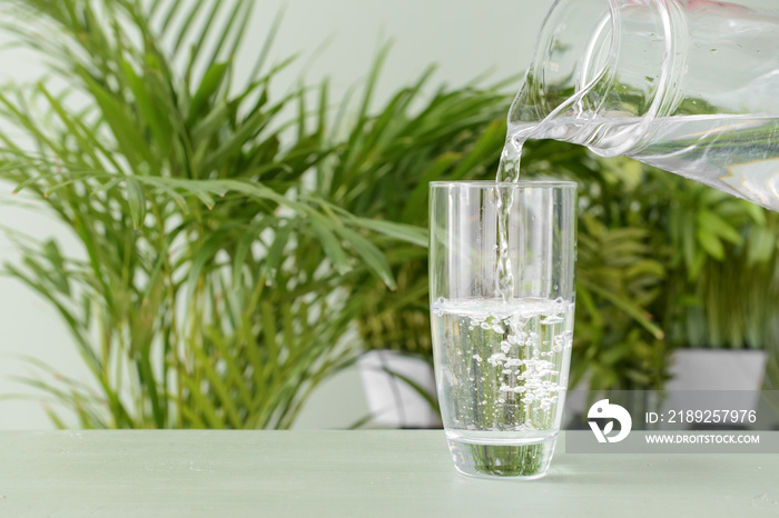 Pouring of fresh water into glass on table