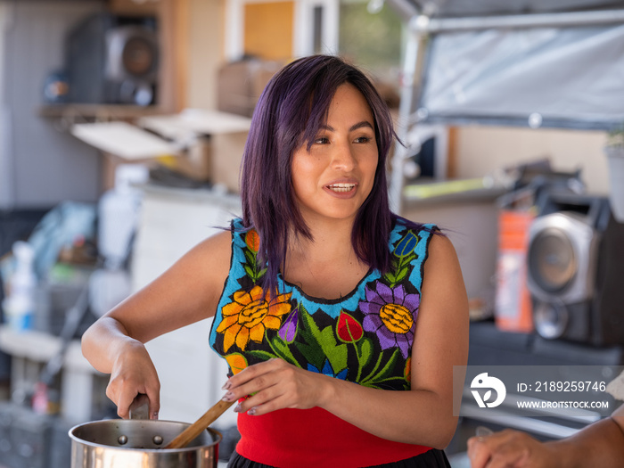 Horizontal image of a young Indigenous woman stirring a pot