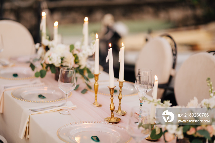 Wedding dinner table at reception. Beautiful white delicate candles burn in metal candlesticks, agai