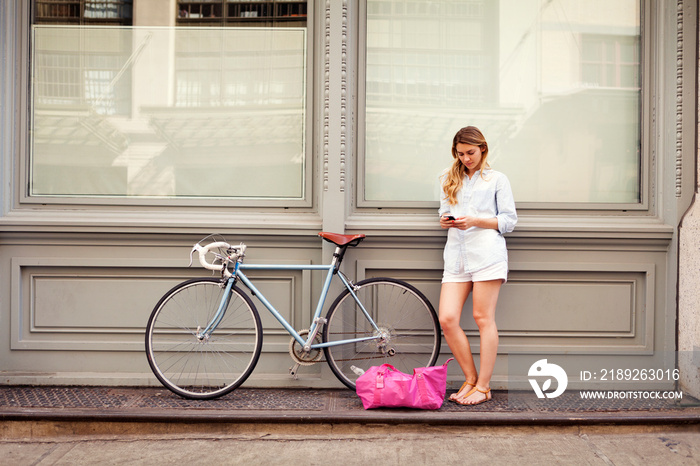 Young woman standing near bicycle and texting message