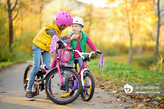 Cute little sisters riding bikes in a city park on sunny autumn day. Active family leisure with kids