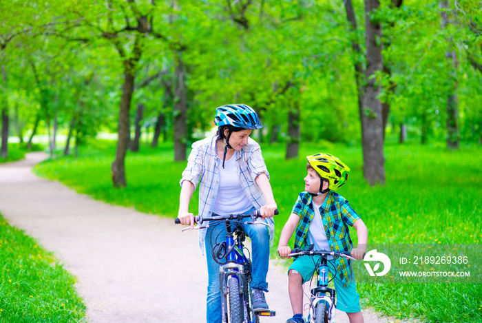 Mom with her son in bicycle helmets ride bicycles and talk on the track in the summer park. Family V