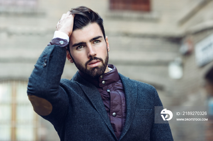 Young bearded man wearing british elegant suit touching his hair