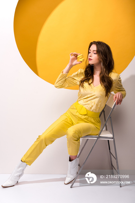 attractive woman sitting on chair and holding macarons on orange and white