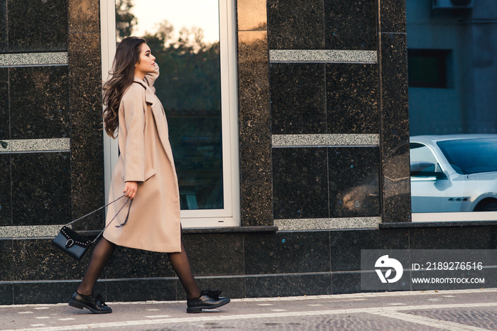 Fashionable woman with long hair walking in the city. Woman wears trendy coat and shoes.