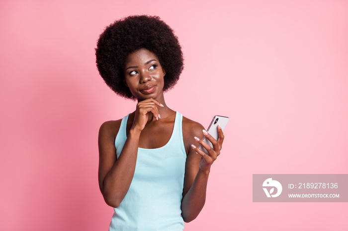 Photo of brunette minded afro american woman look empty space hold hand chin phone isolated on pink 