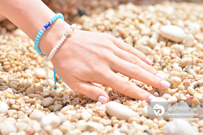 Girls hand with a fashion summer bracelet in nautical style on a sea pebbles