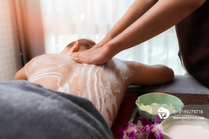 Spa therapist applying scrub salt and cream on young woman back at salon spa. Hands massaging female