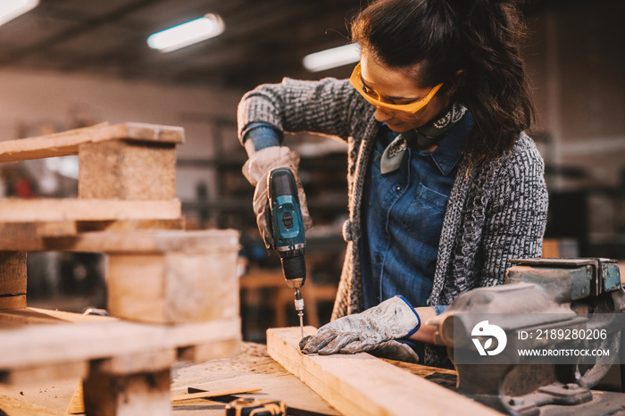 Female carpenter using drill while working in workshop. Female doing males work concept.