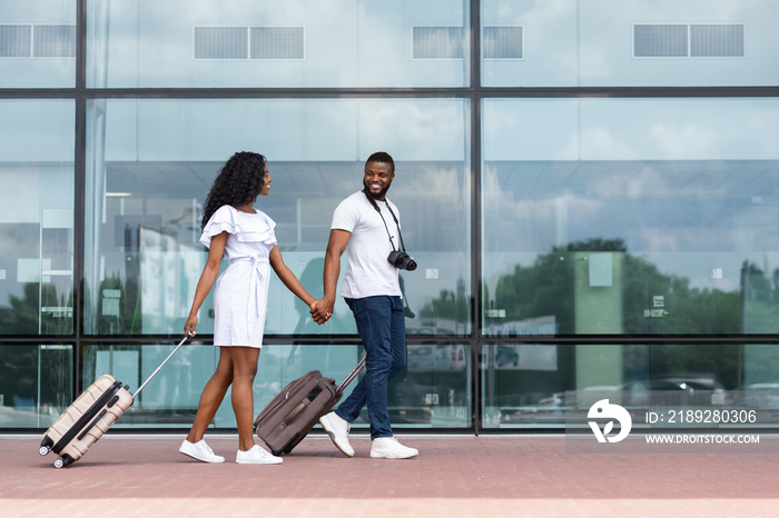 African couple walking with luggage near airport building