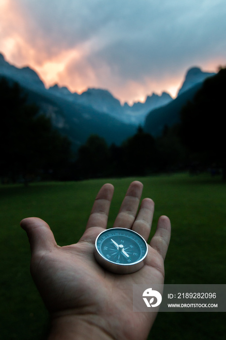 Compass held with one hand in a mountainous landscape. Traveler exploring new places and escaping in