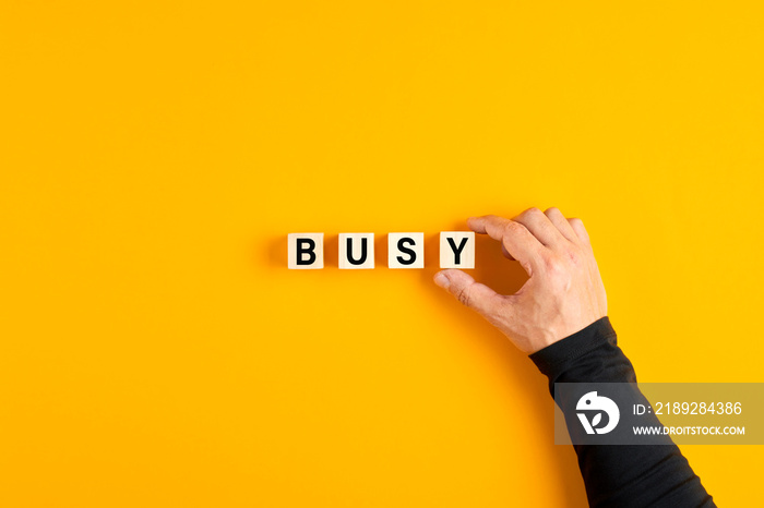 Male hand placing the wooden cubes with the word busy on yellow background. Overwork, stress or occu