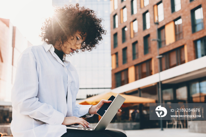 Close up photo of a busy caucasian it worker sitting on a bench and using a laptop while wearing eye