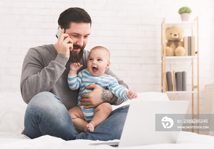 Young dad working on laptop at home with his baby son