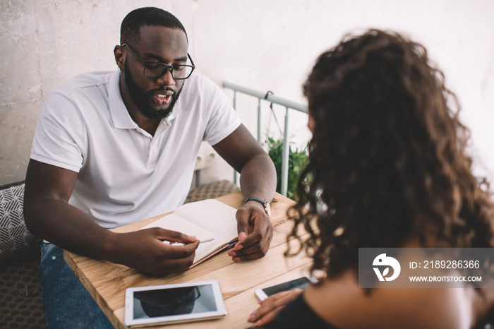 Focused black student showing note to colleague in cafe