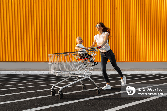 excited young woman with child, with shopping trolley on yellow wall of shopping mall, family shoppi