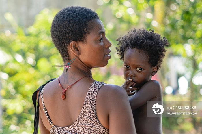 Imagen horizontal de una mujer africana de espalda cargando a su pequeño hijo al aire libre en un dí