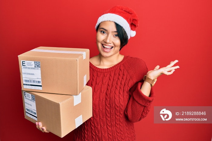 Beautiful young woman with short hair wearing christmas hat holding delivery packages celebrating vi