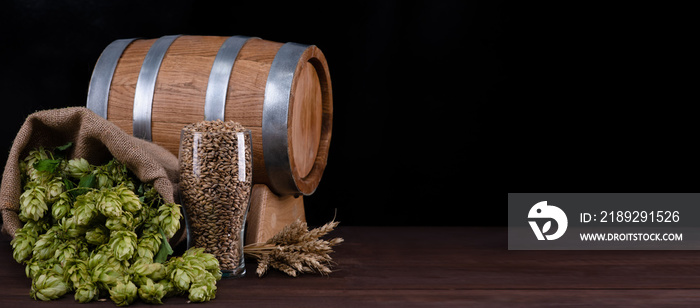 Homebrewing concept. Barrel and beer glass with malt, wheat and fresh green hops in sackcloth bag on