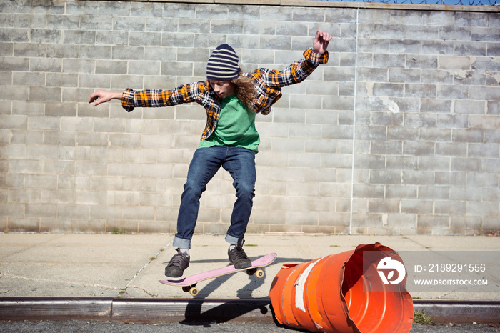 Young man skateboarding against gray wall