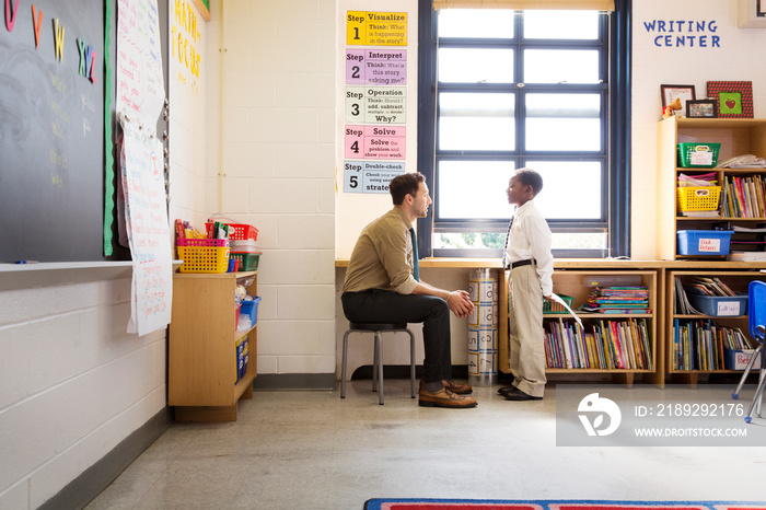 Teacher talking to schoolboy in classroom