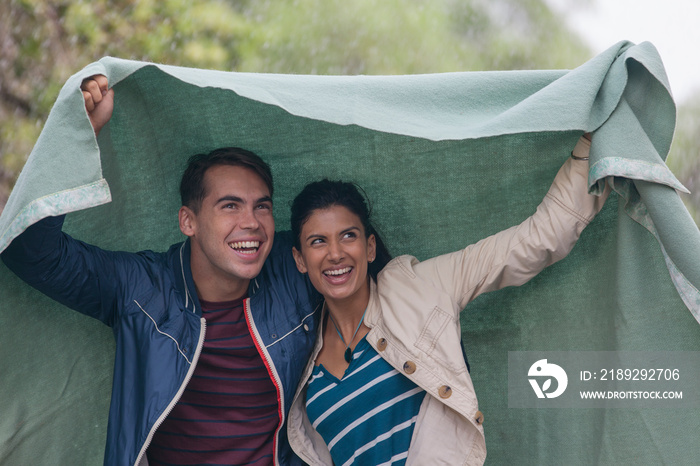 Happy young couple under blanket in rain