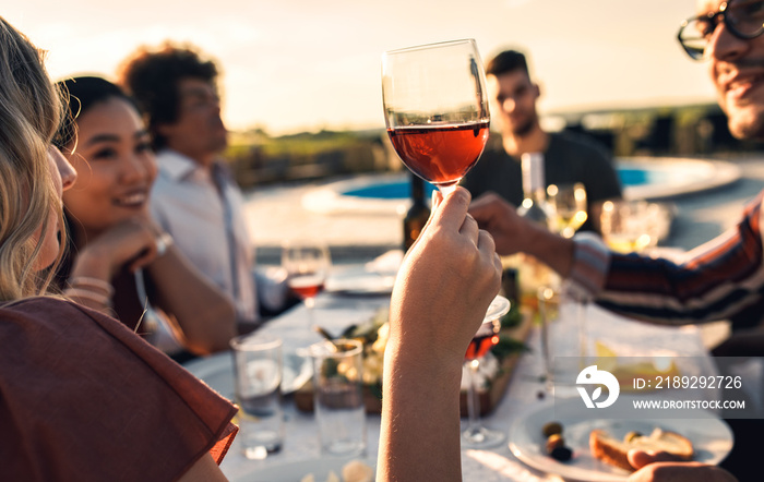 Close up of woman hand holding a glass of red wine at dinner party with her friends.