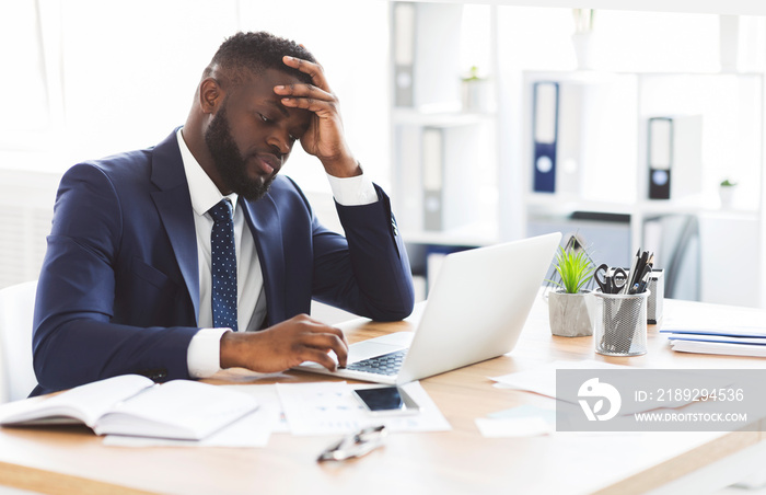 Exhausted young entrepreneur working with laptop in office