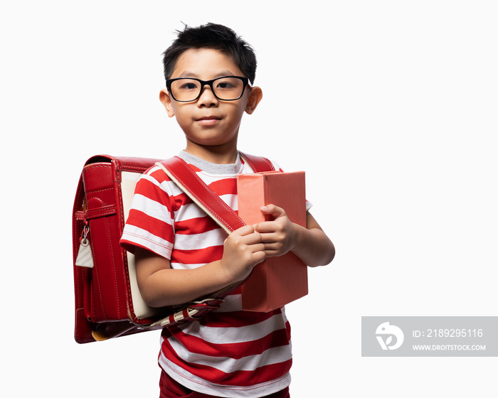 Happy cute clever boy in glasses with school bag and book in his hand. Modern backpack. Child is rea