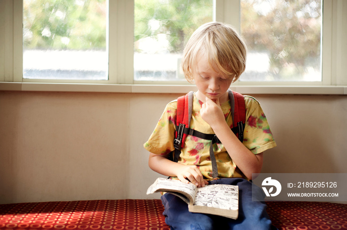 Boy (6-7) reading by window