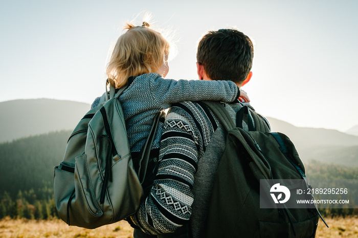 Father and child with a backpack enjoying the sunset in the mountains.The concept of family travel, 