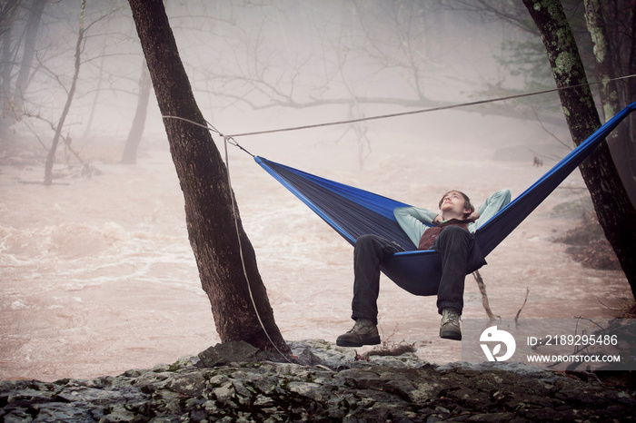 Young male hiker relaxing in hammock next to river