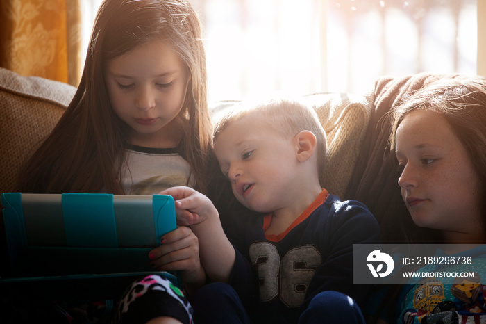 Siblings (2-3, 10-11) sitting on sofa and using tablet pc