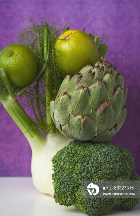 A fennel bulb, limes, an artichoke, and a head of broccoli