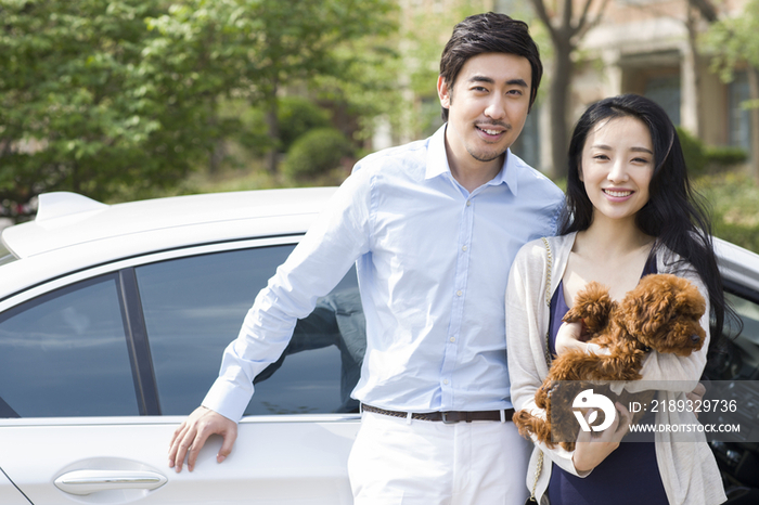 年轻夫妇抱着宠物狗站在车旁