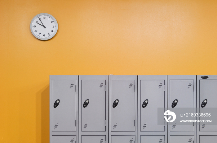 Clock on an orange wall above lockers, in a modern secondary school