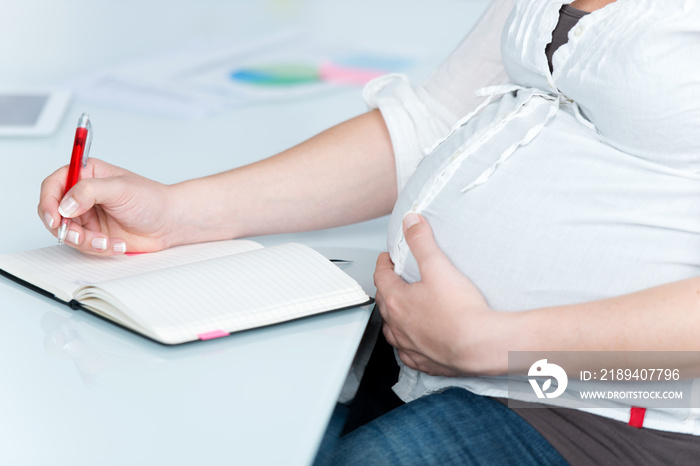 schwangere frau schreibt etwas in ihren kalender