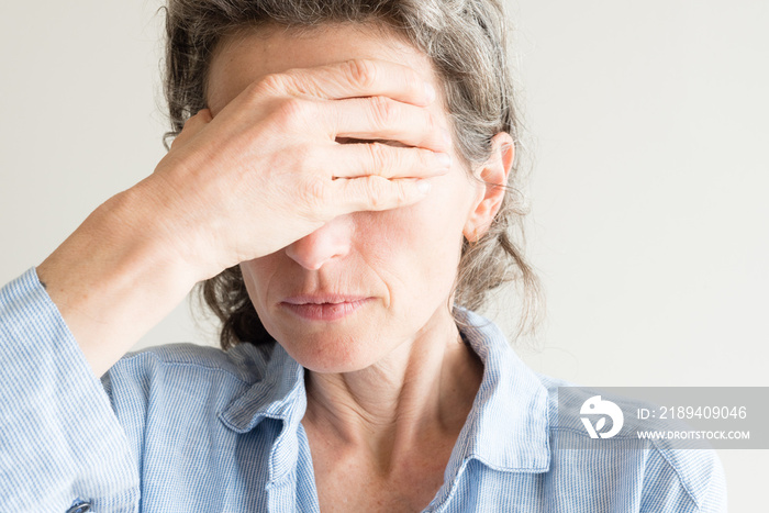 Close up of middle aged woman with hand covering eyes