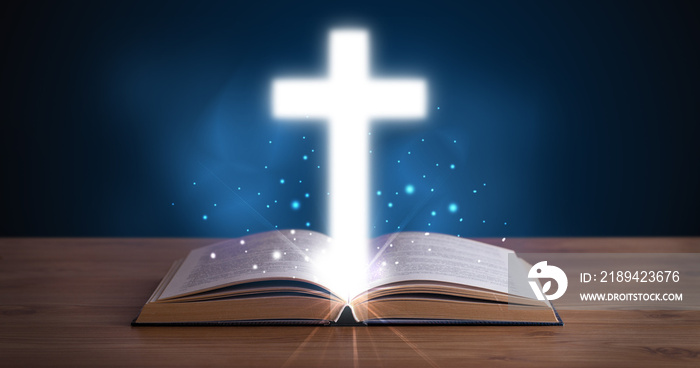 Open holy bible with glowing cross in the middle