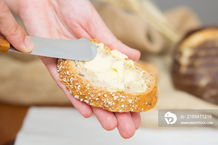 女人用刀在法棍面包片上抹黄油的手。特写镜头。传统面包