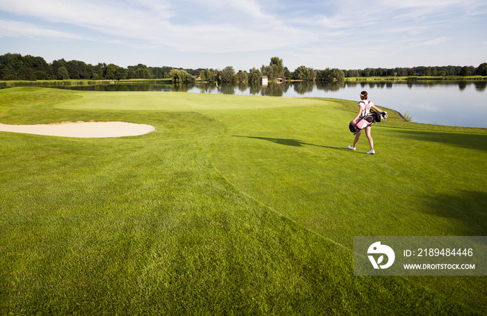 女孩高尔夫球手走在高尔夫球场与高尔夫球袋。