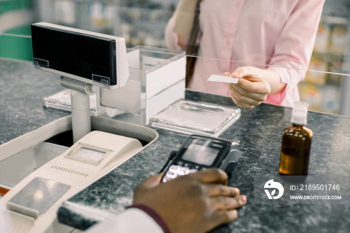 Customer woman making payment in drugstore. Pharmacist holding terminal, woman paying for drugs with