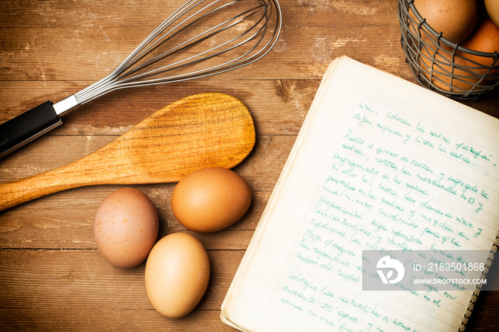 Receta de cocina junto con huevos, cuchara, batidora y cuaderno sobre una mesa de madera rústica. Vi