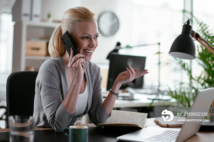 Businesswoman using phone. Happy young woman talking on smartphone in office.