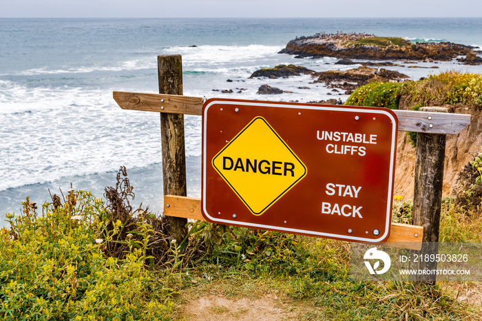 Danger, unstable cliffs, stay back  sign posted on the Pacific Ocean coastline on an area with erode