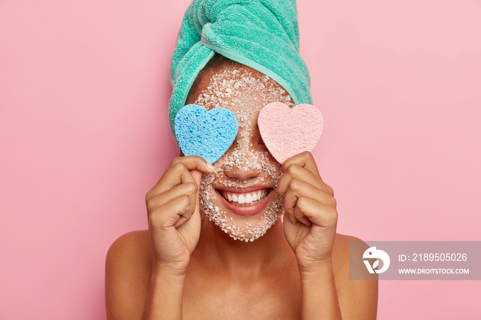 积极的深色皮肤女性在美容护理中玩得很开心，眼睛上戴着两块心形海绵